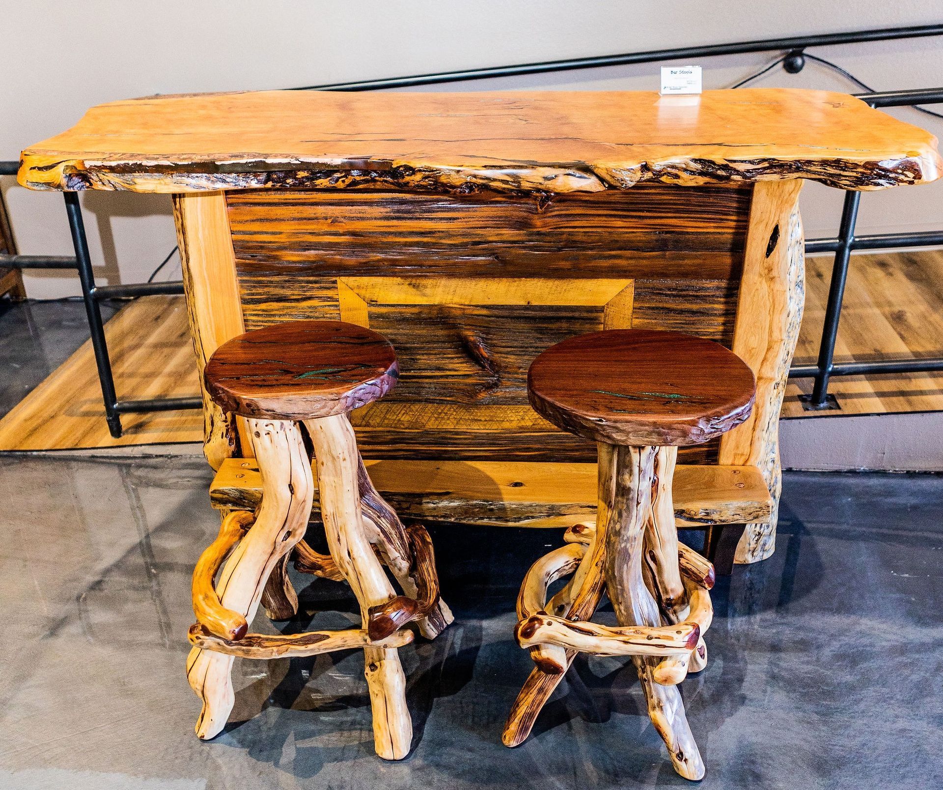A rustic wooden bar with a live-edge top and two matching twig-style stools standing on a dark floor.