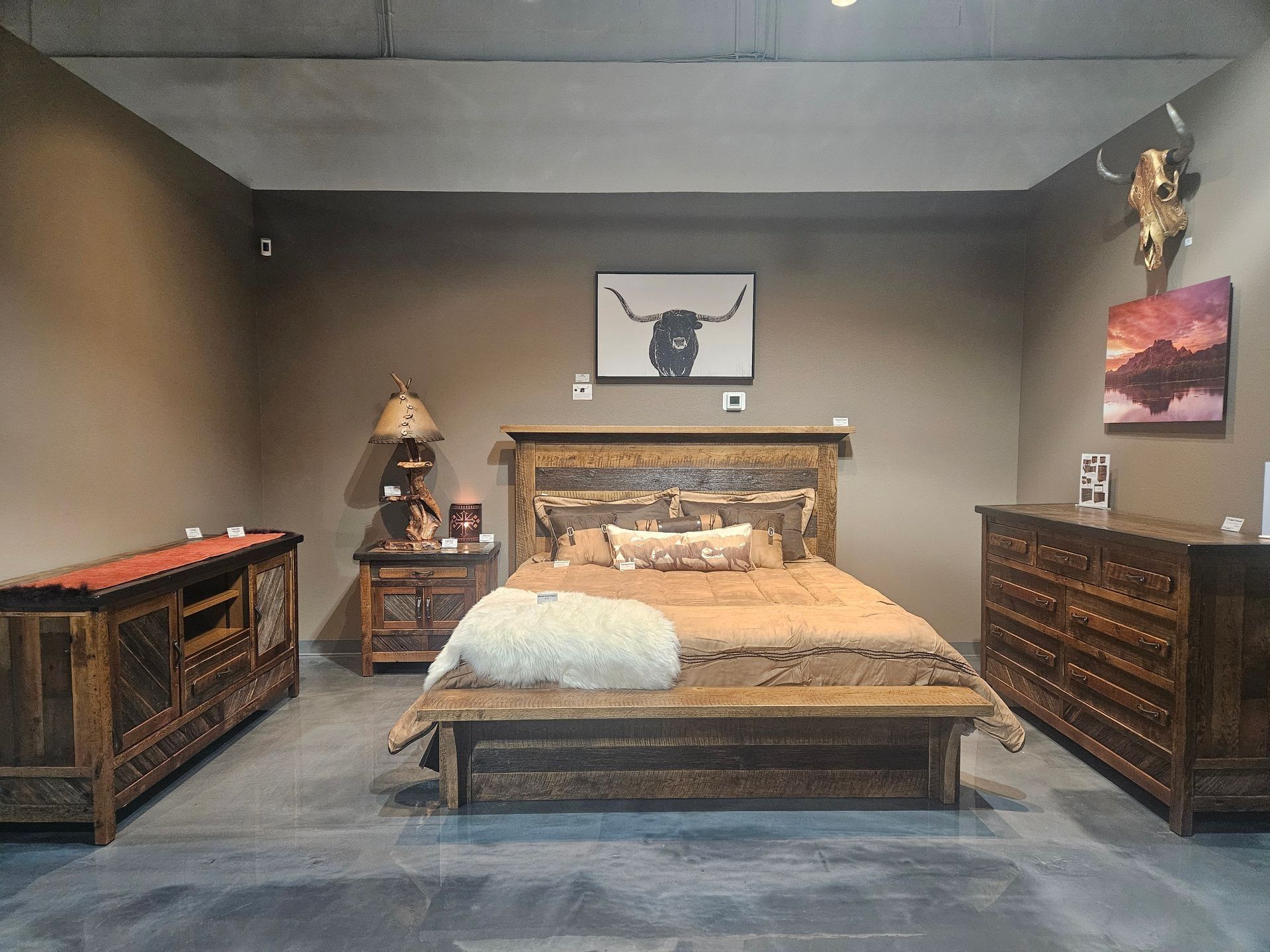 A room with a rustic recliner, a cow-print accent chair, a matching lamp with a base, and a small cow portrait on the wall.