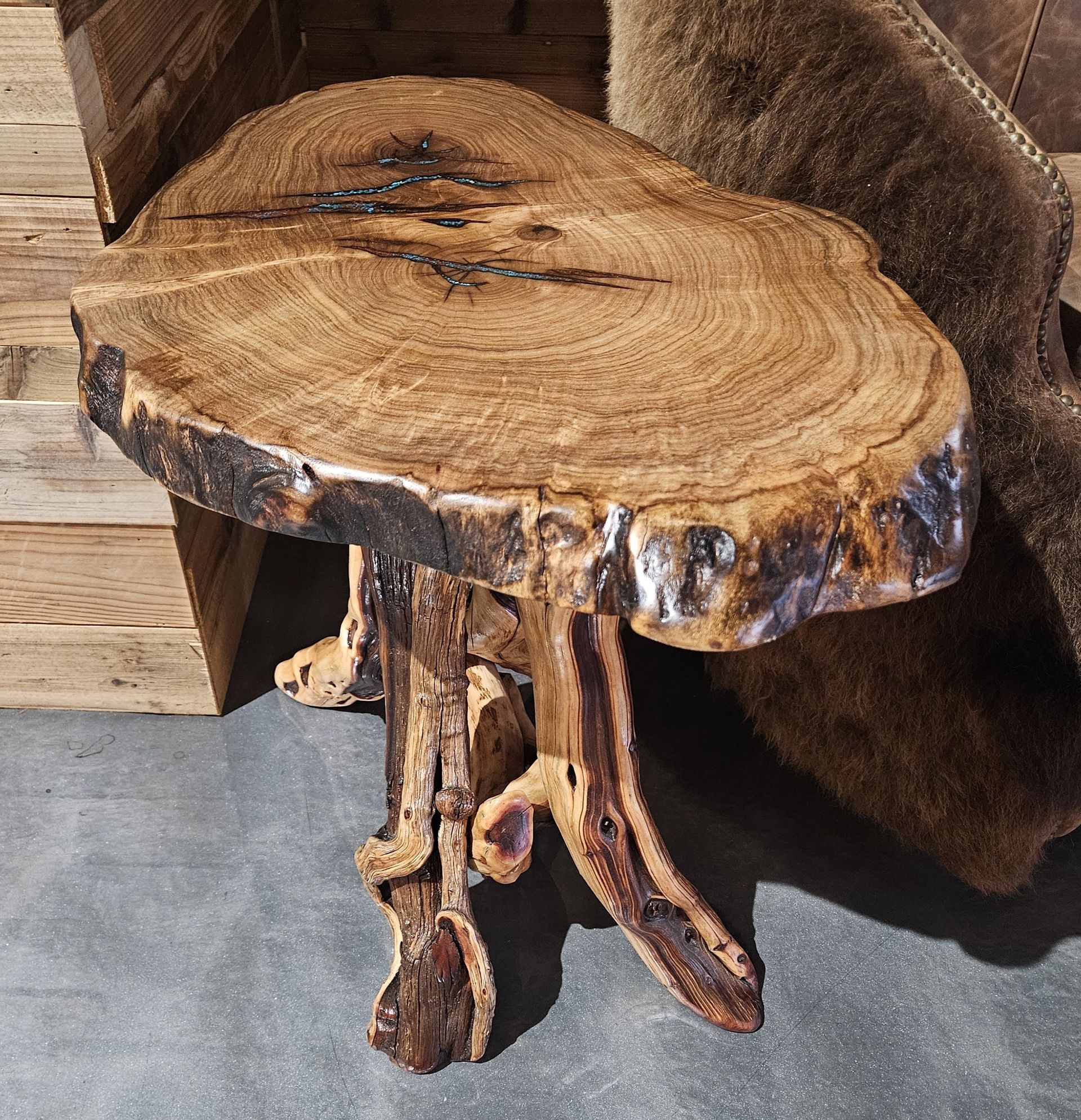 A rustic side table with a raw-edged circular wood slab top resting on a tripod base made from natural tree roots.