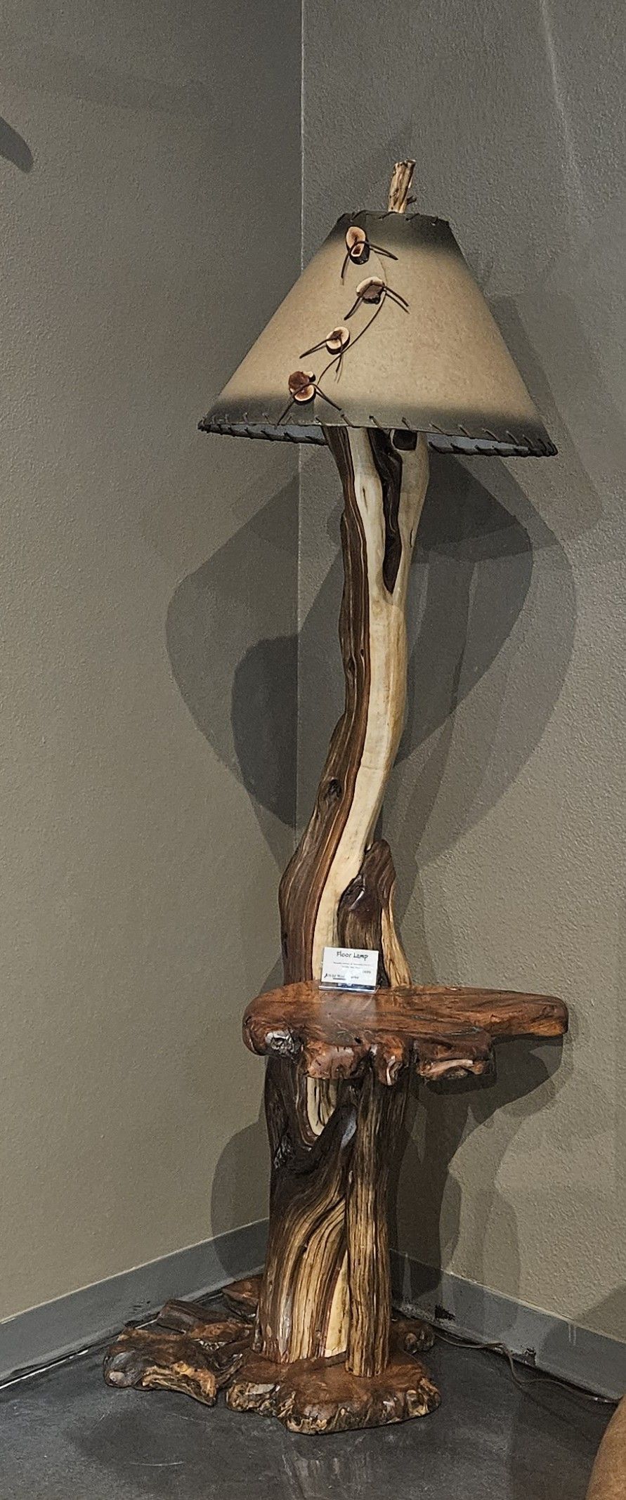 A rustic floor lamp with a driftwood-style base, a small wooden shelf, and a textured, cone-shaped lampshade.