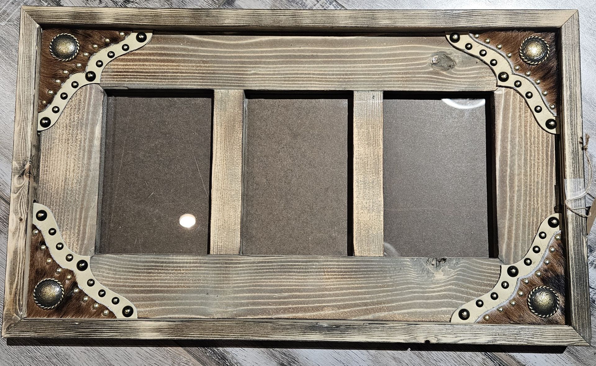 A rustic, rectangular wooden picture frame for three photos, featuring decorative metal corners with stud accents.