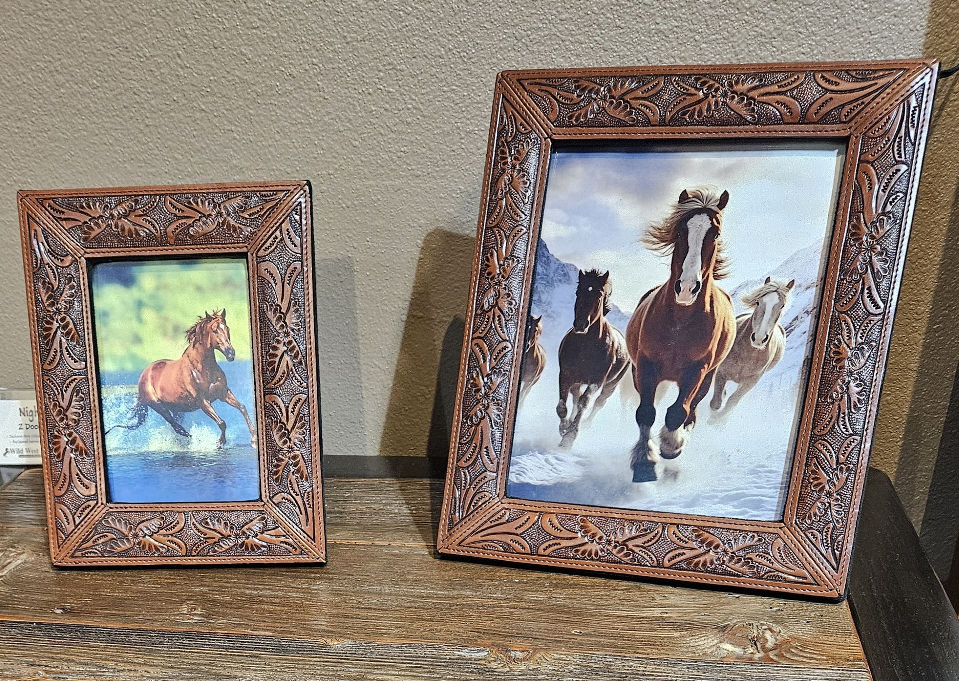 Two ornate, western-style picture frames displaying horse artwork sit on a mottled brown surface.