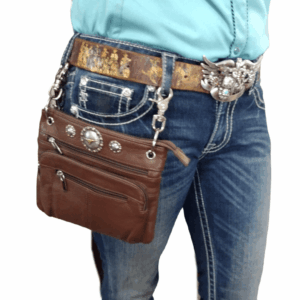 A brown leather purse hangs from a belt with a large metal buckle, attached to blue jeans with silver metal clips.