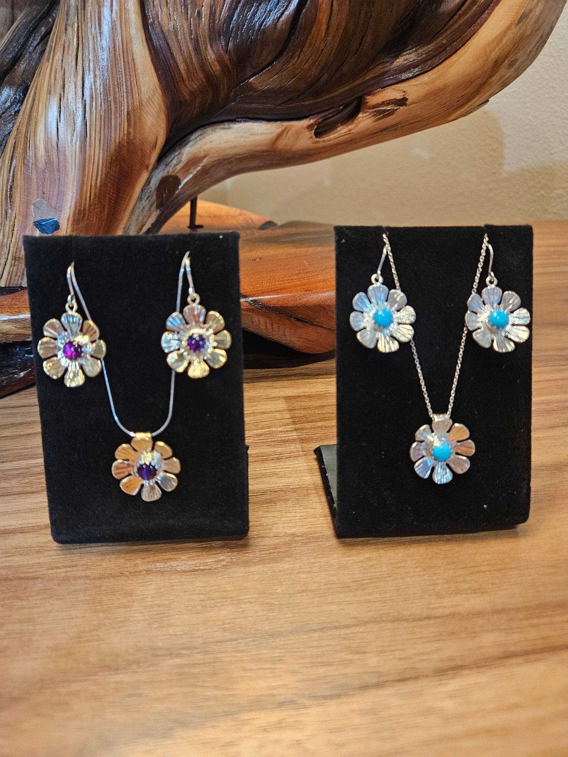 Two floral jewelry sets on black display stands, featuring silver flower petals with purple or turquoise centers.