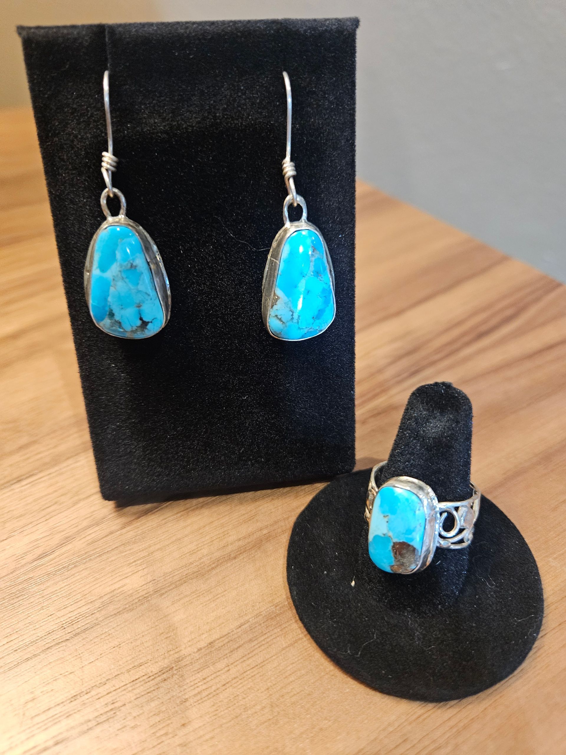 Turquoise and silver jewelry set with matching teardrop earrings on a black stand and a ring on a black display base.
