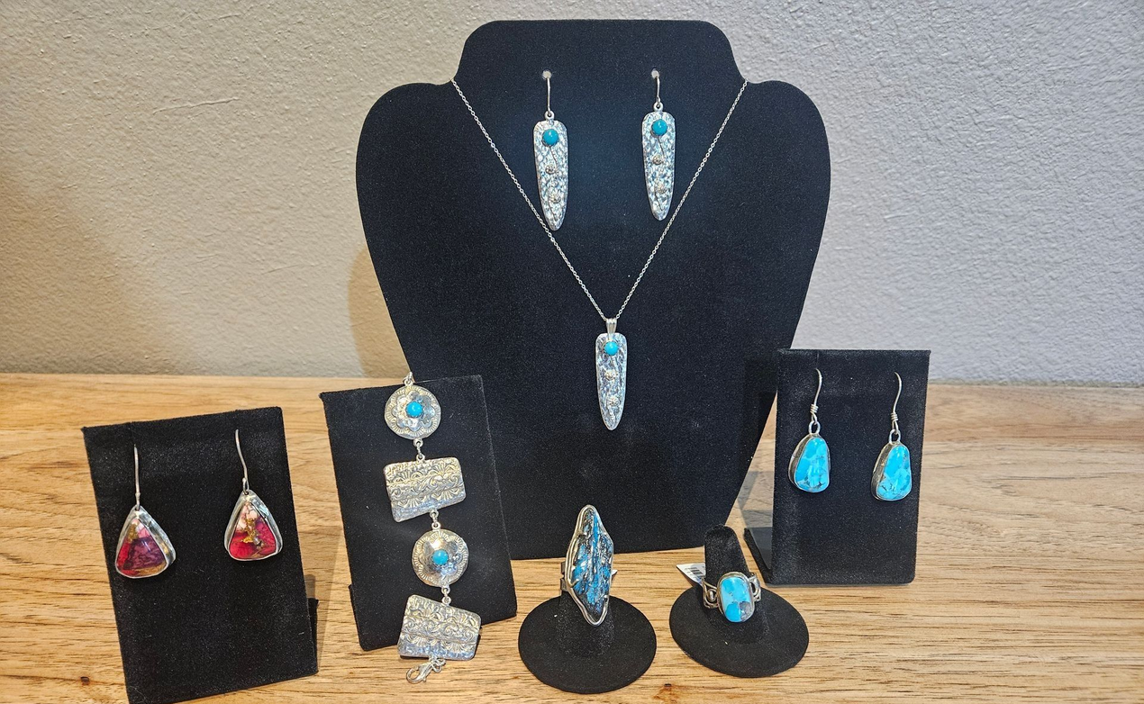 A collection of turquoise and silver jewelry, including necklaces, earrings, and rings, displayed on black stands.