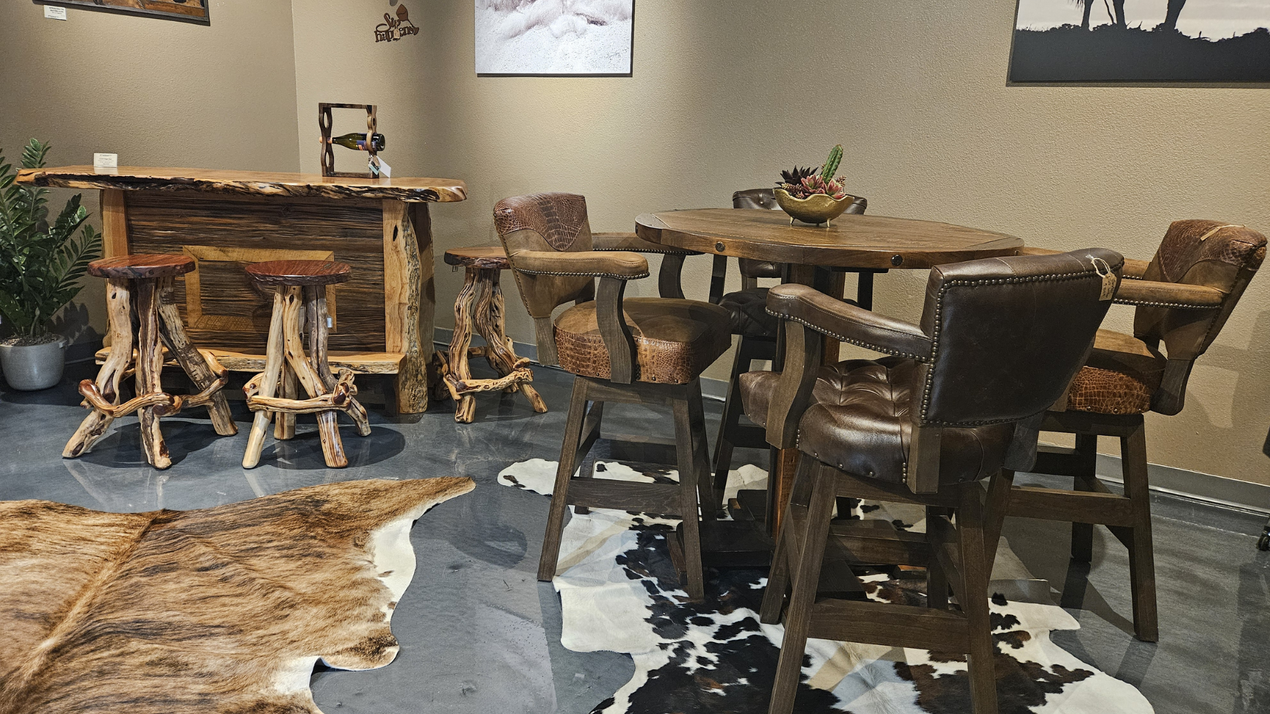 Rustic café seating with wooden tables and chairs on a stone floor, with plants and a counter in the background.