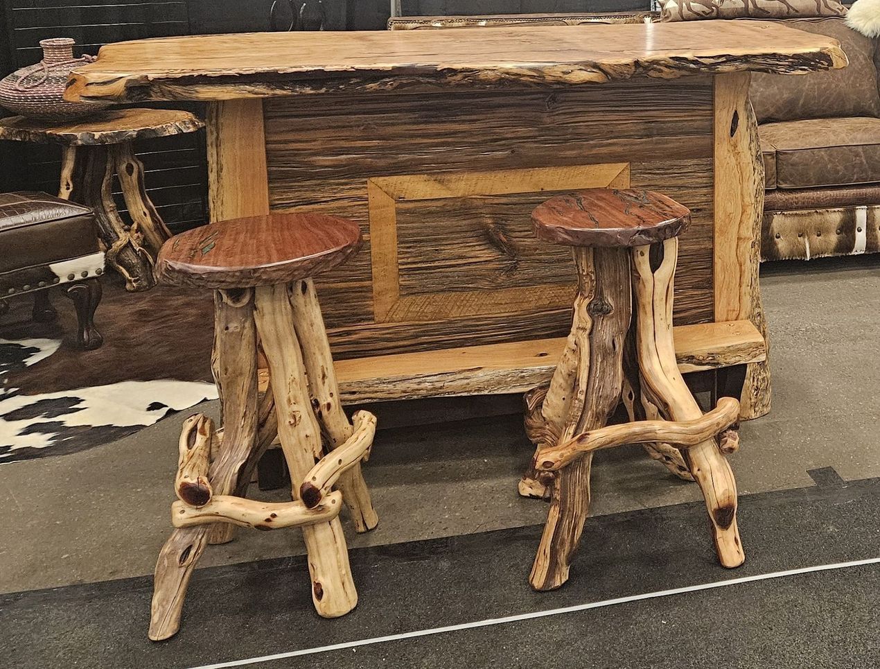 A rustic wooden bar with a live-edge countertop and two matching stools featuring natural branch legs and dark seats.