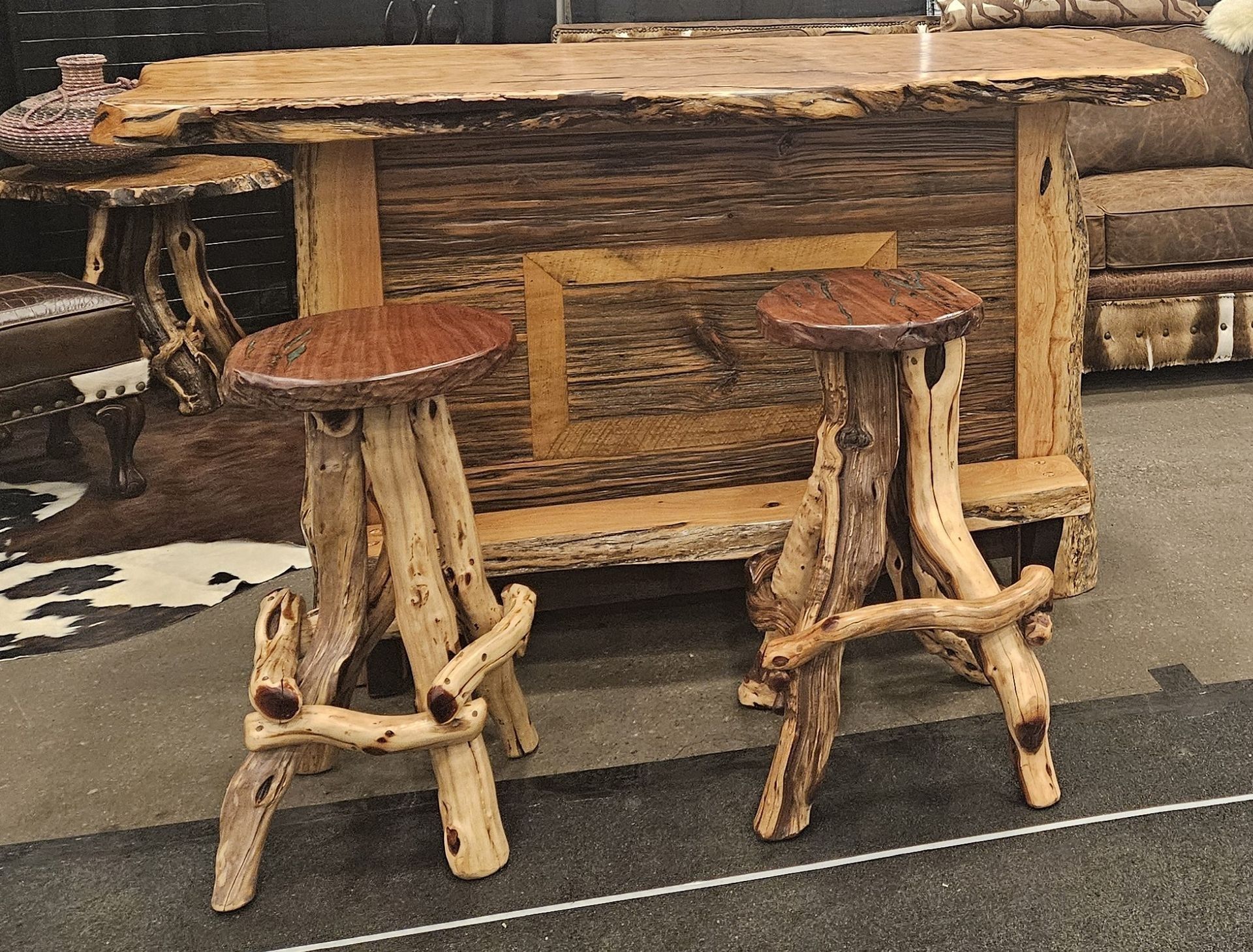A rustic wooden bar with a live-edge countertop and two matching stools featuring natural branch legs and dark seats.