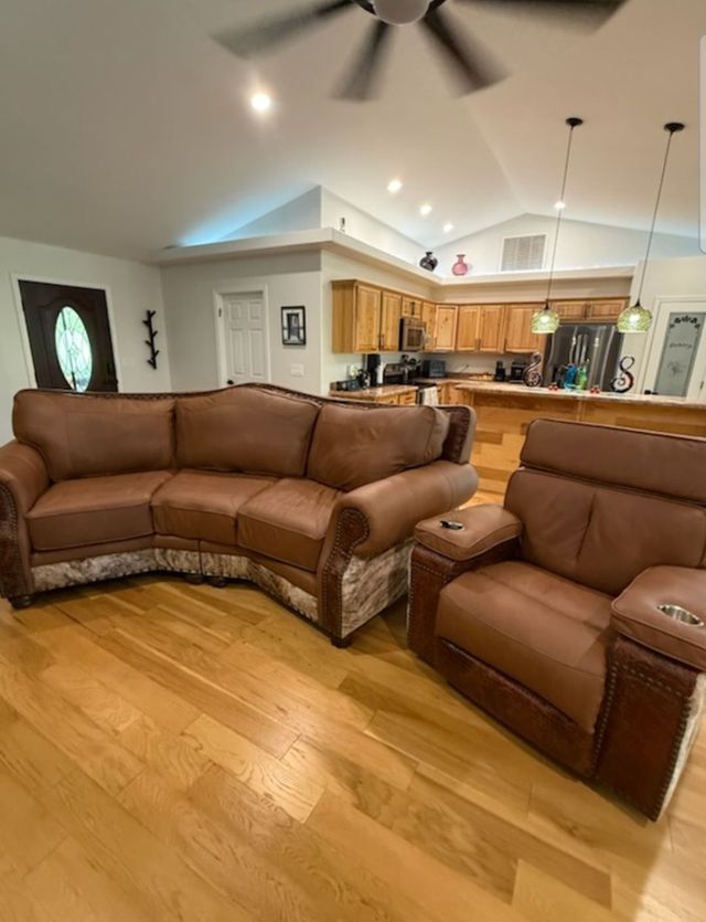 Living room with brown sectional and recliner, hardwood floor, open kitchen, and ceiling fan lights.
