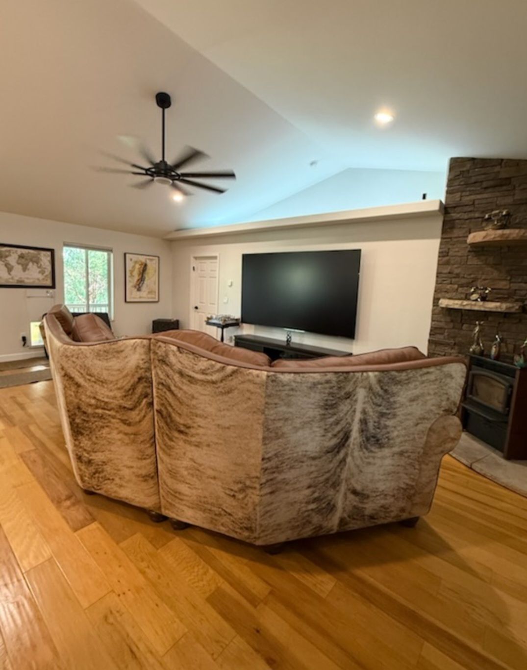 Living room with sectional sofa, large TV, stone fireplace, and hardwood floors.