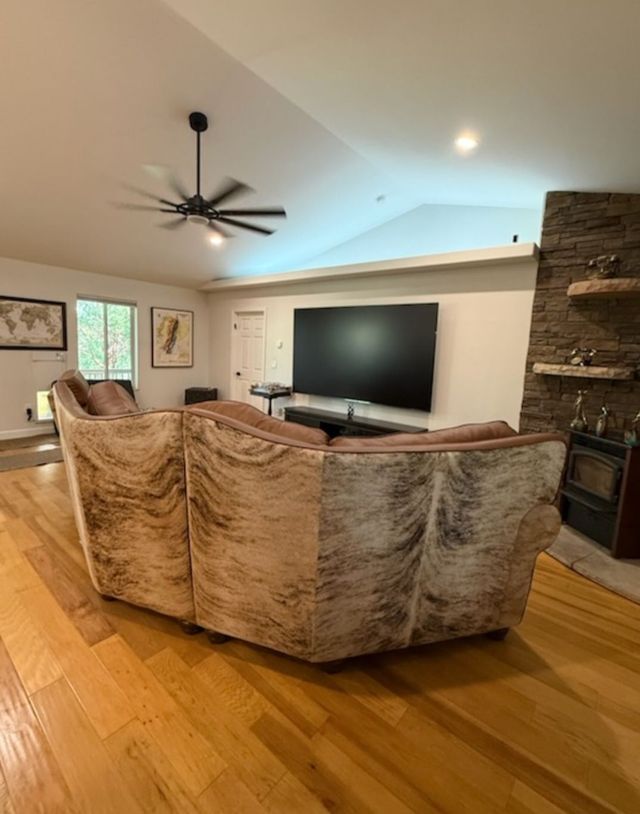 Living room with sectional sofa, large TV, stone fireplace, and hardwood floors.
