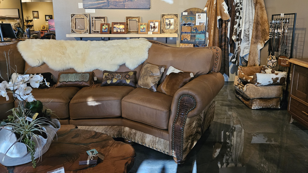 A rustic western-style living area features a leather chair with cowhide accents, wood tables, and animal skull wall decor.