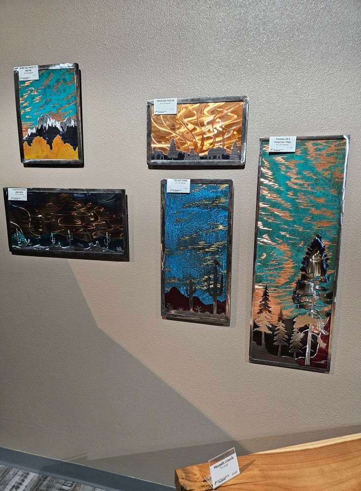 Metal landscape art pieces with colorful backgrounds mounted on a wall.