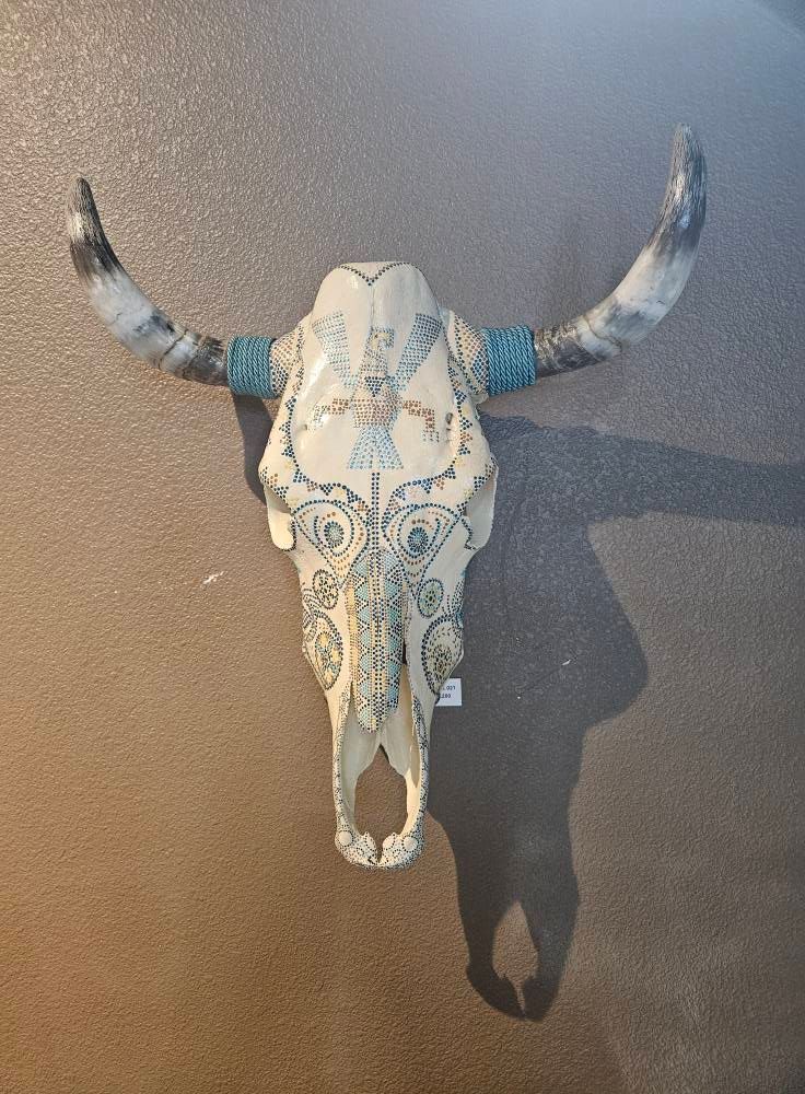 Decorated cow skull with turquoise accents and intricate design on a tan wall.