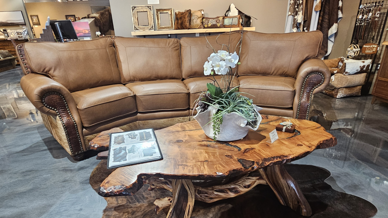 A room with a rustic recliner, a cow-print accent chair, a matching lamp with a base, and a small cow portrait on the wall.