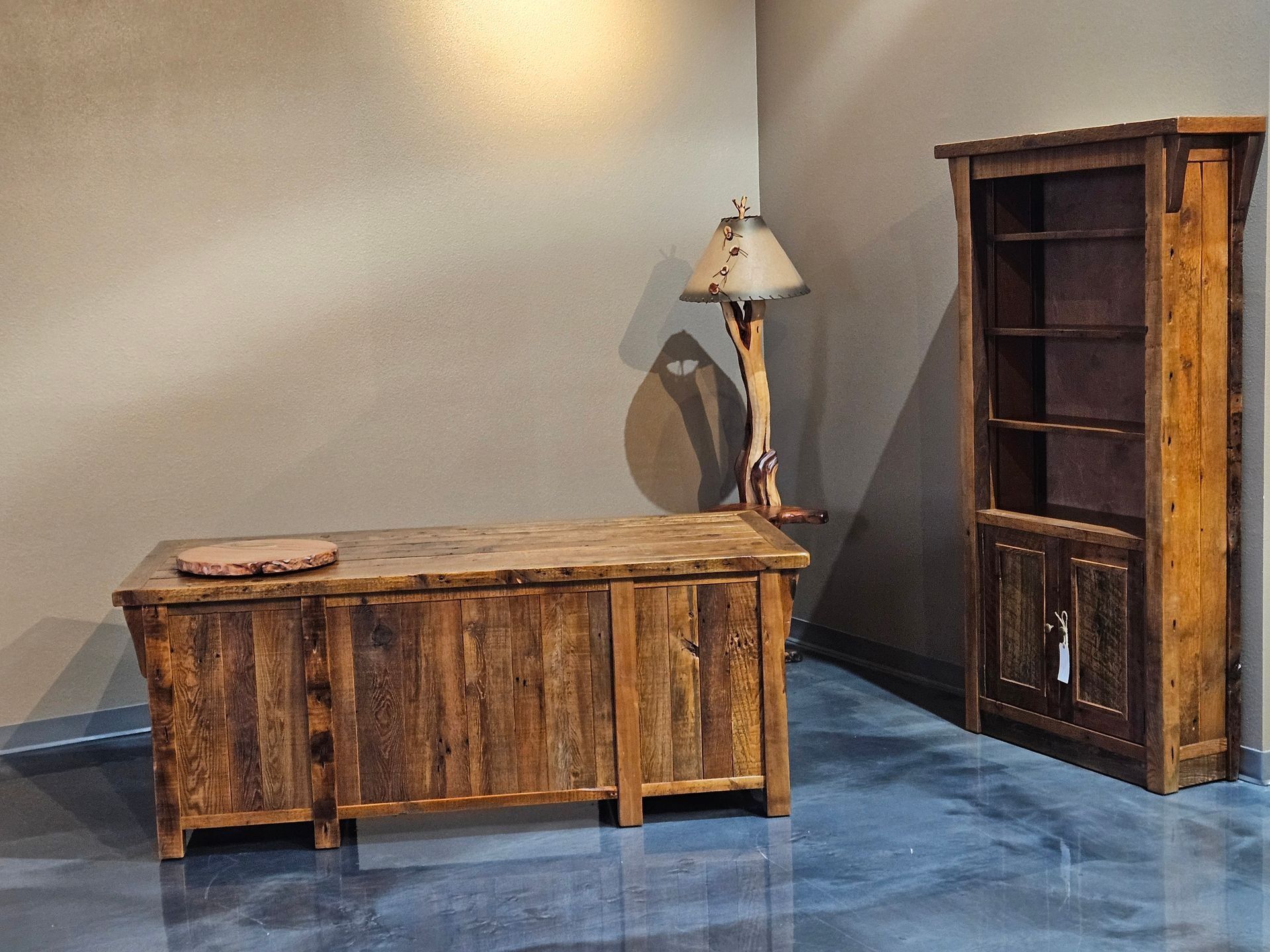 Rustic wooden desk and bookcase in a corner with a decorative lamp.