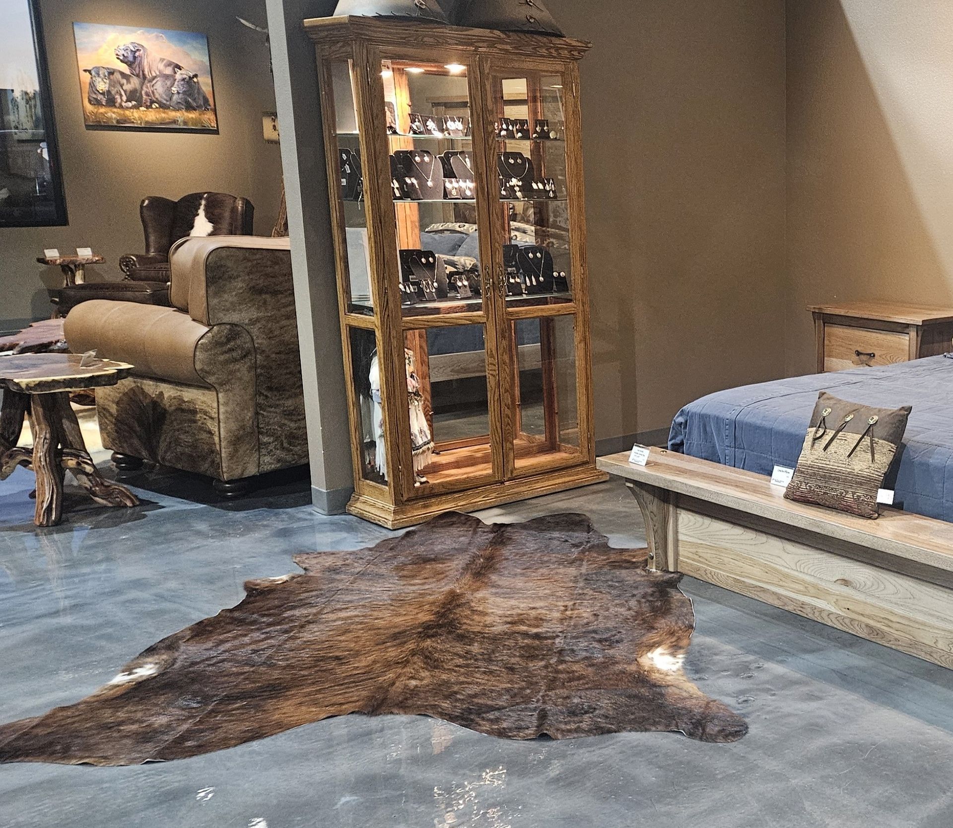 A rustic furniture showroom with a wood display cabinet, cowhide rug, armchair, and a bed with a patterned pillow.