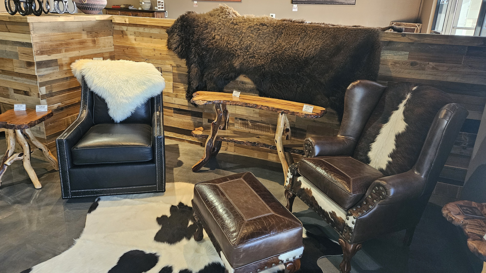 Cozy living room with dark leather chairs, fur throw, wooden bench, and black-and-white cowhide rug.