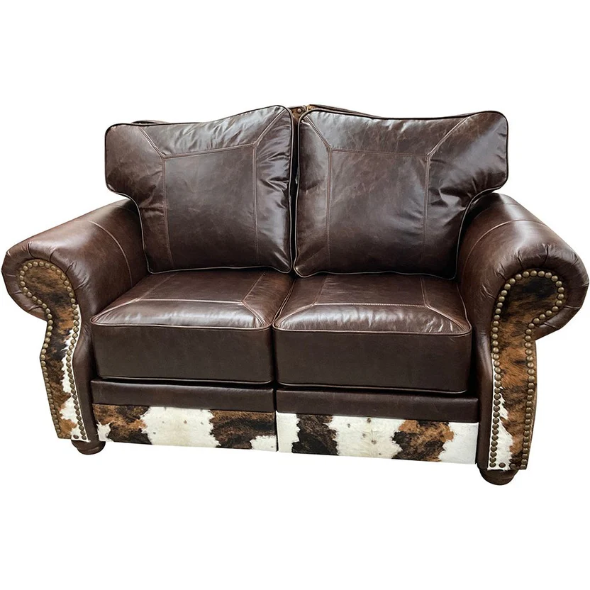 A brown leather loveseat with cowhide trim on the arms and base, featuring rolled arms and decorative metal nailheads.