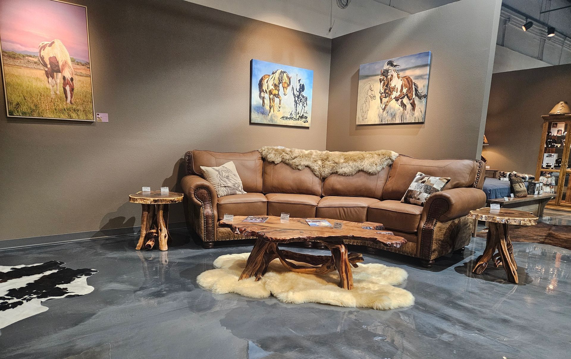 A room with a rustic recliner, a cow-print accent chair, a matching lamp with a base, and a small cow portrait on the wall.