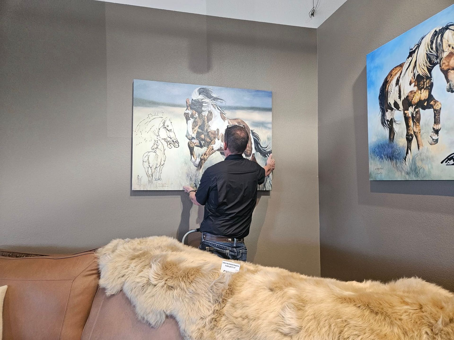 A room with a rustic recliner, a cow-print accent chair, a matching lamp with a base, and a small cow portrait on the wall.