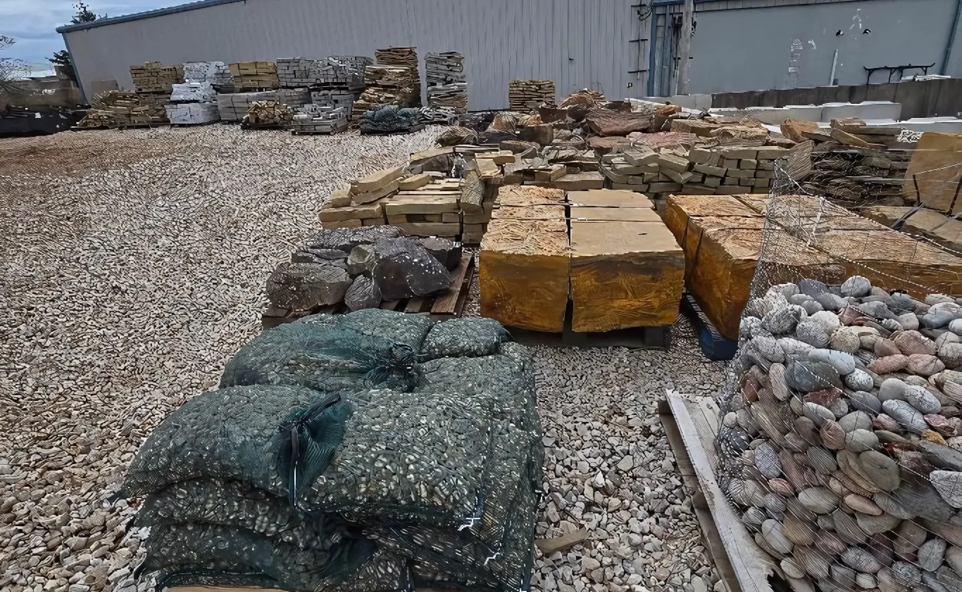 Stacks of landscaping stone and gravel pallets in an outdoor yard beside a warehouse.