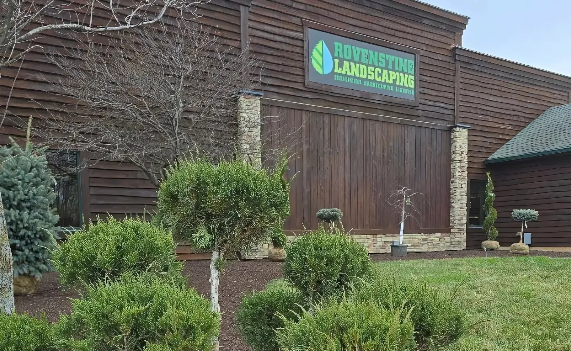 Brick office building with a green-and-blue sign above the entrance and trimmed shrubs in front
