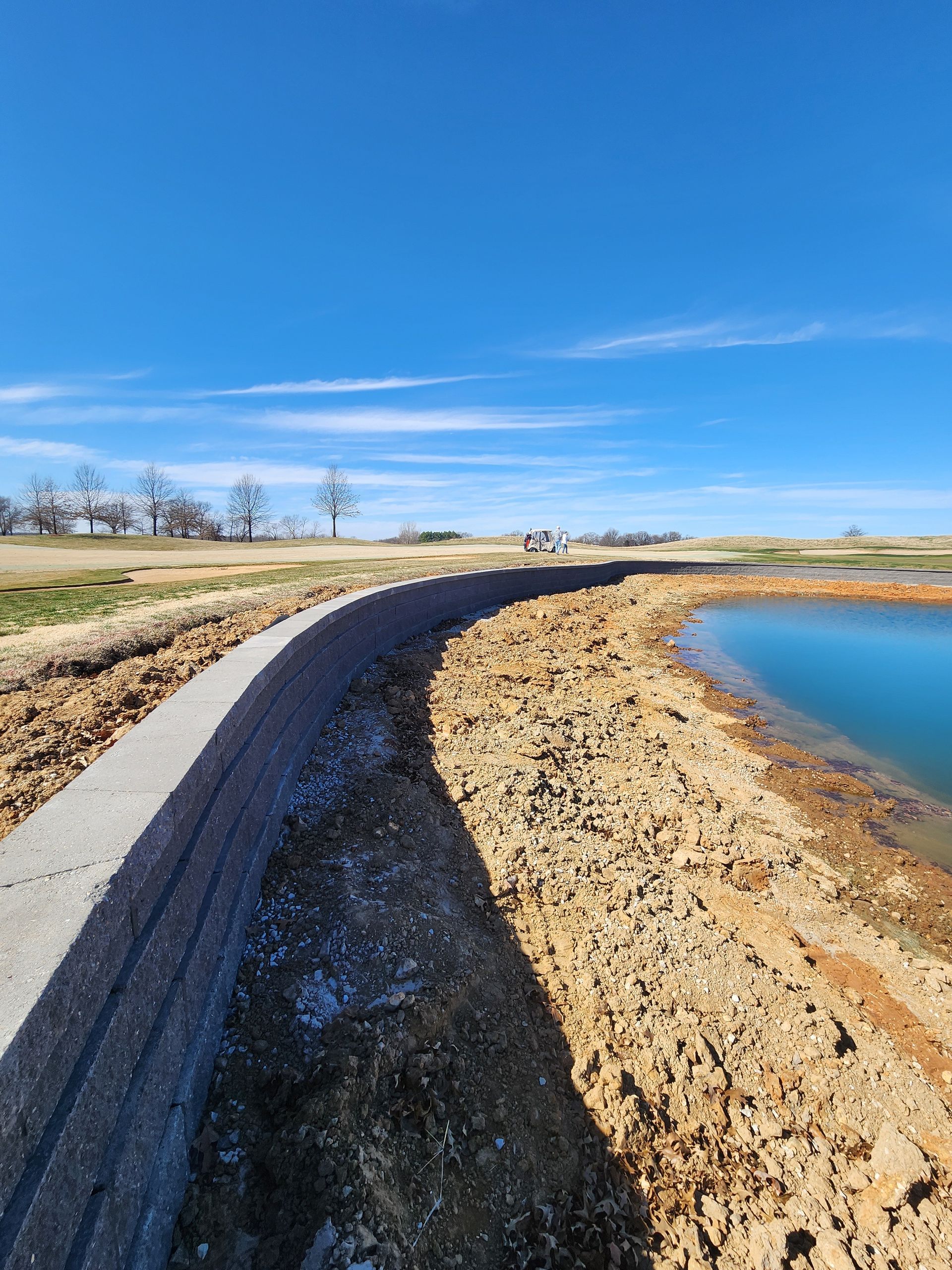 Curving dirt road beside a blue pond under a clear blue sky
