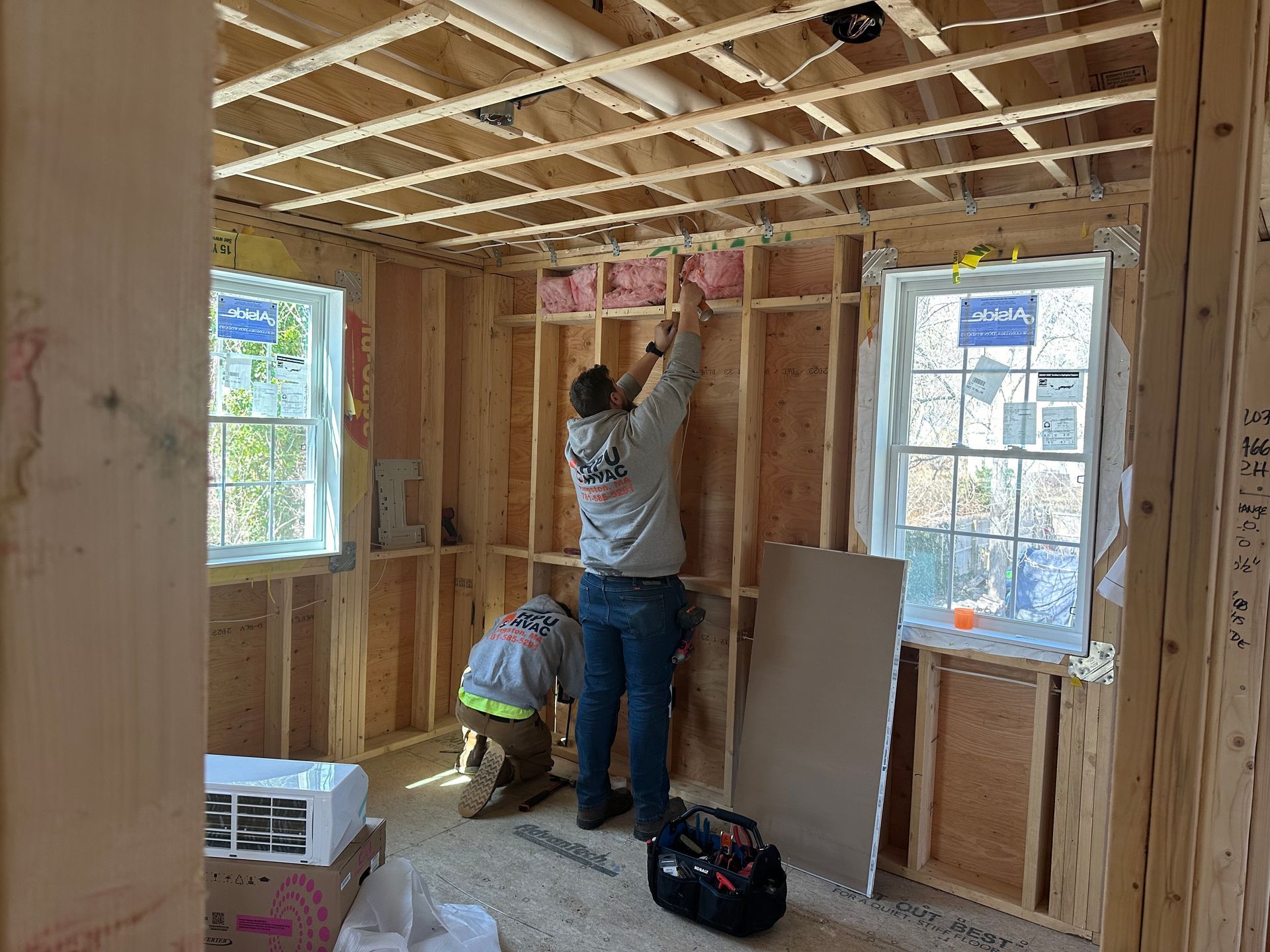 Two men are installing air condition in a room under construction