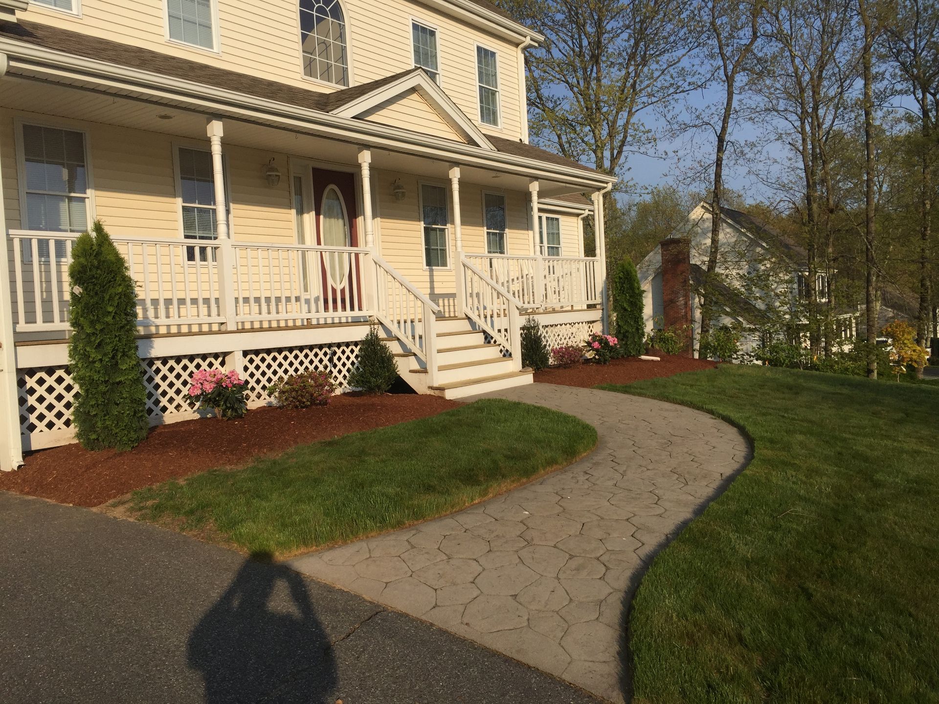 A light yellow house with a covered front porch and stone-patterned walkway set in a sunny, green residential yard.