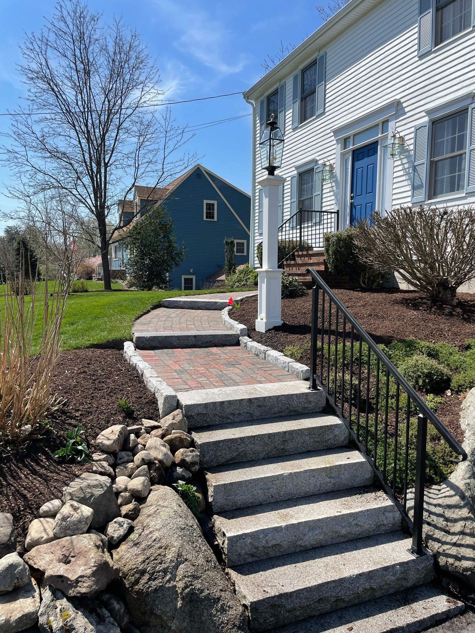 A stone staircase with a black metal railing leads up to the front entrance of a white house with a blue door.