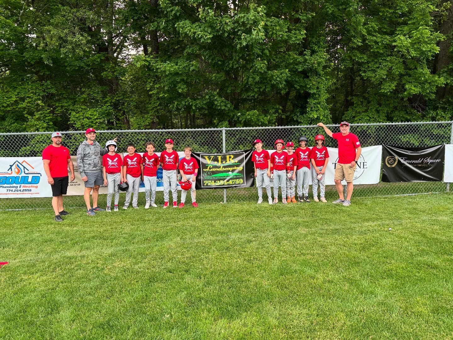 Youth baseball team in red jerseys poses on a field with coaches.