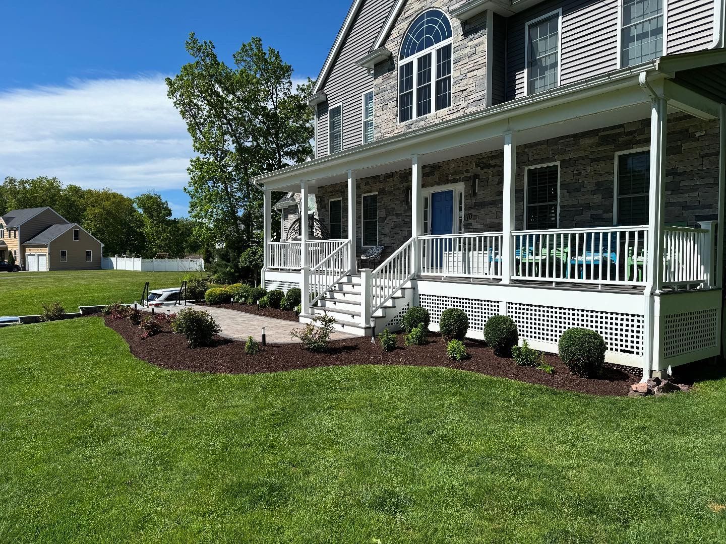 A two-story house with a porch. Landscaping with mulch and shrubs surrounds the porch, green grass in front.