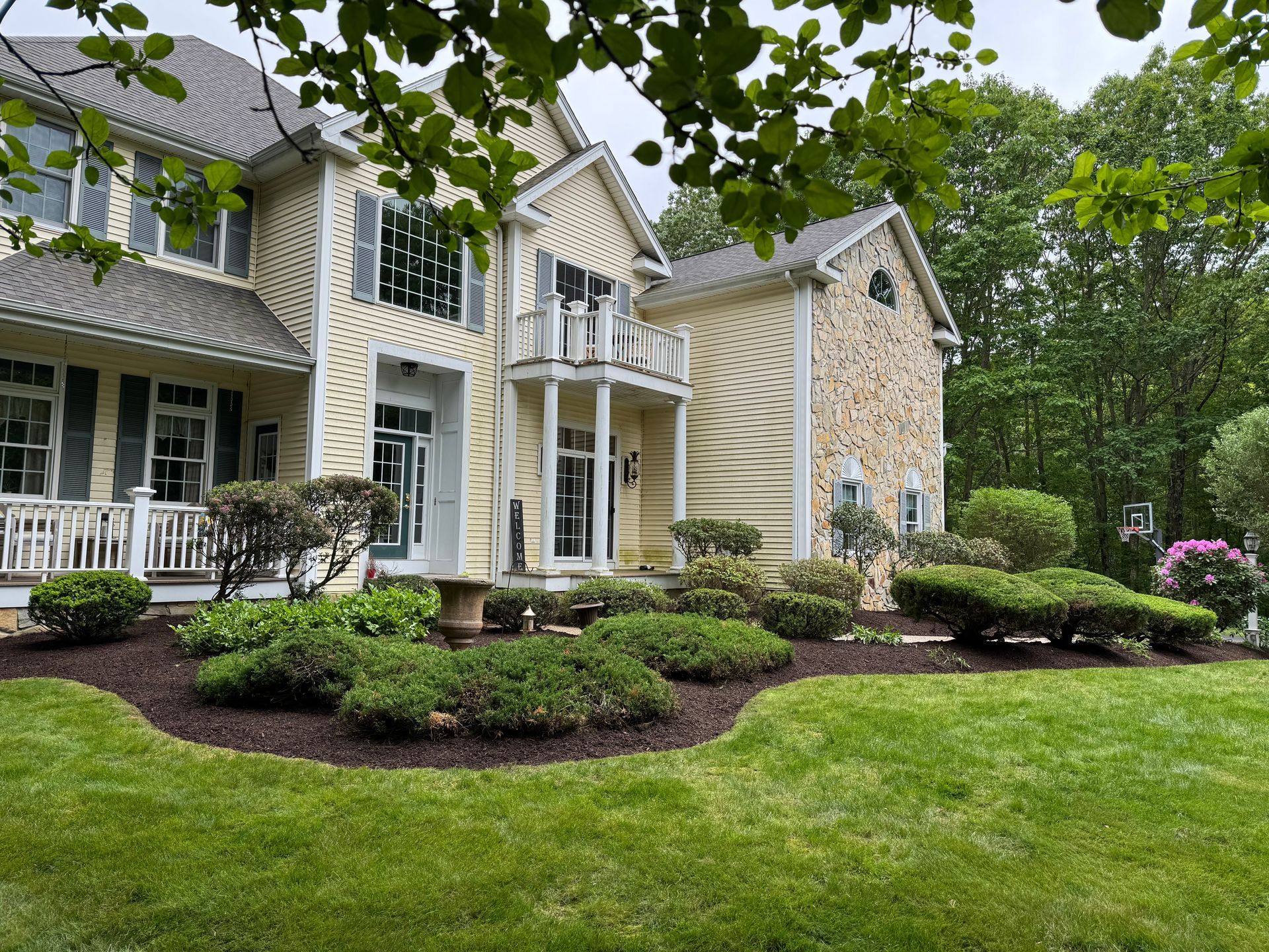 Yellow house with stone accents, lush landscaping, and green lawn.