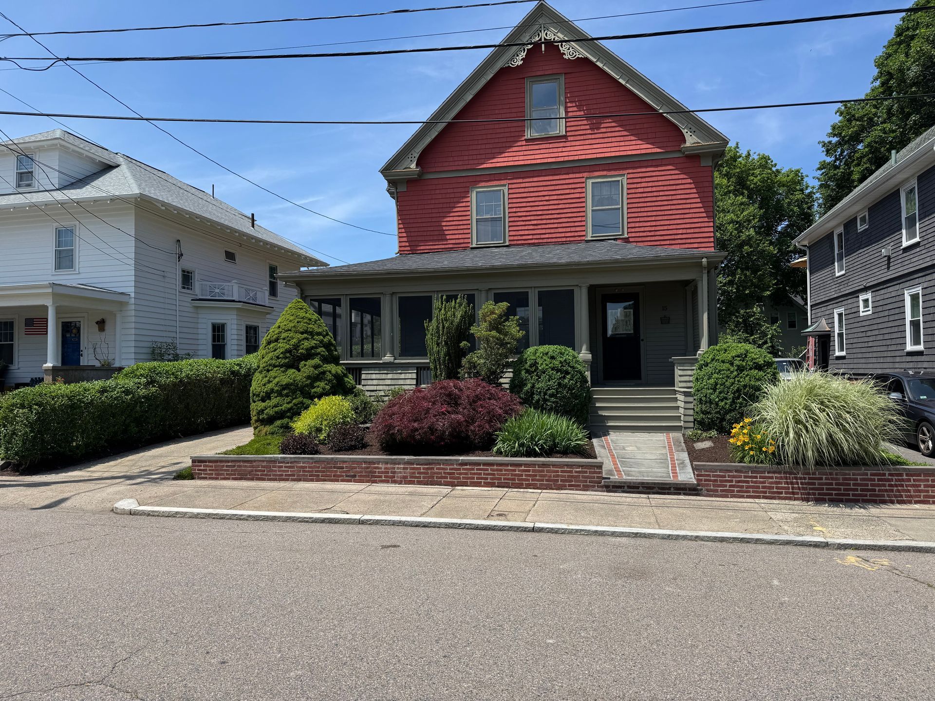 Two-story red house with porch, landscaping, and a sidewalk; sunny day.