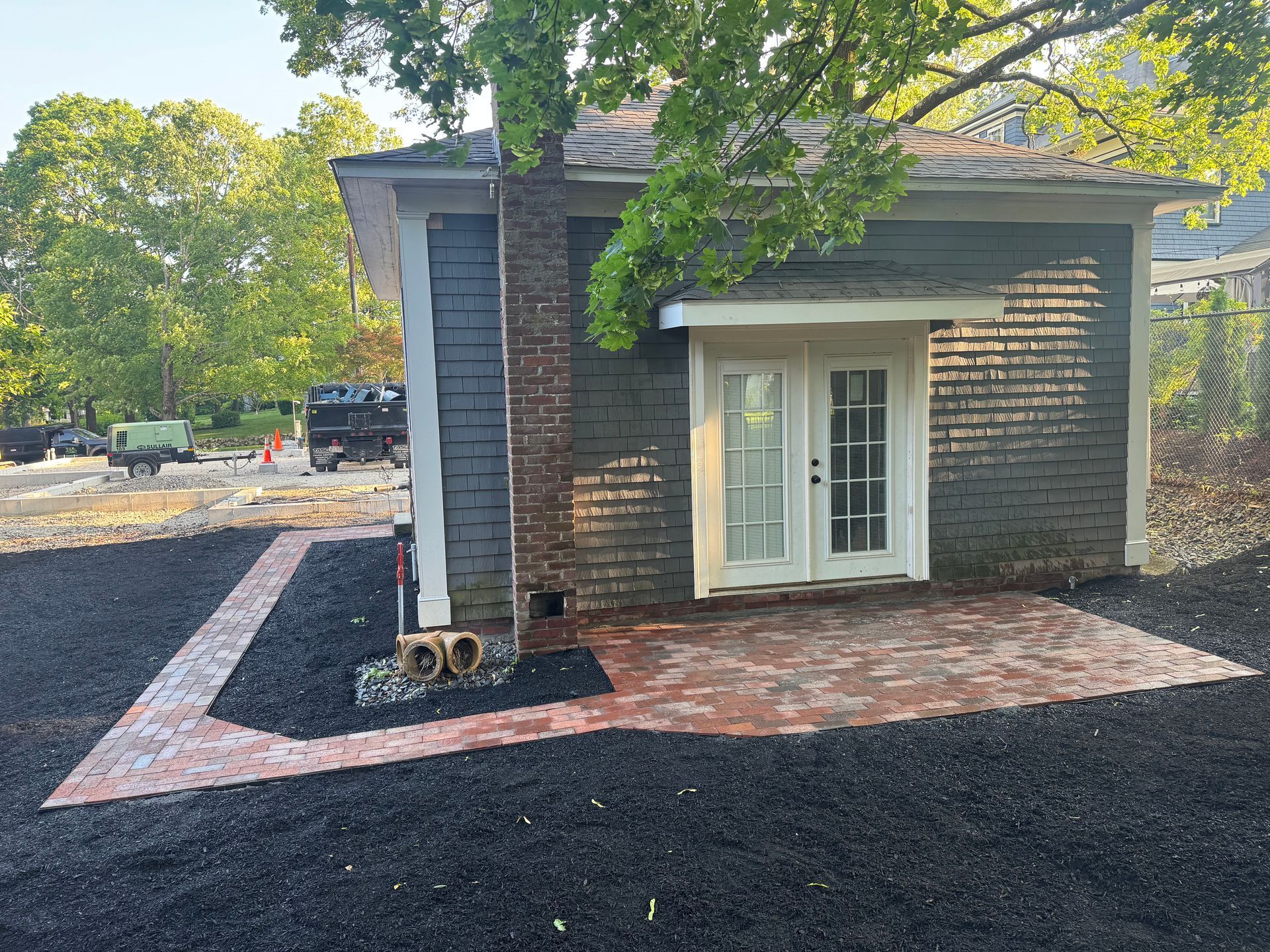 Brick patio with French doors, dark blue siding, and a brick chimney surrounded by black mulch.