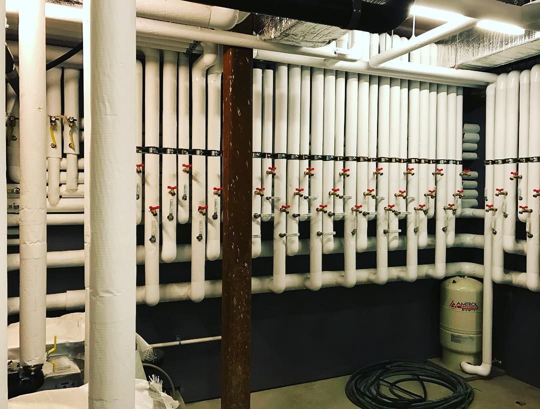 A blue boiler is sitting in a room next to a black wall.