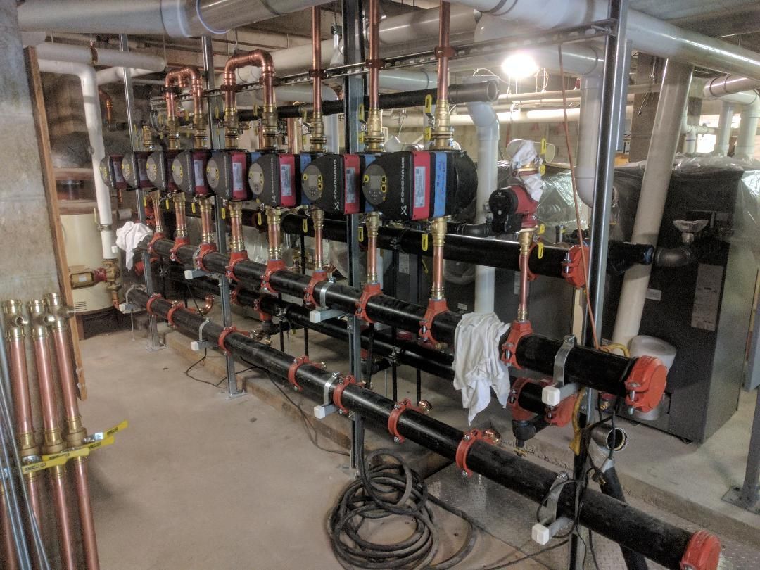 A blue boiler is sitting in a room next to a black wall.