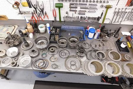 Disassembled car transmission parts laid out on a workbench in a workshop.