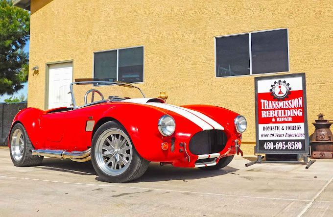 Red classic car with white stripes parked in front of a transmission repair shop.