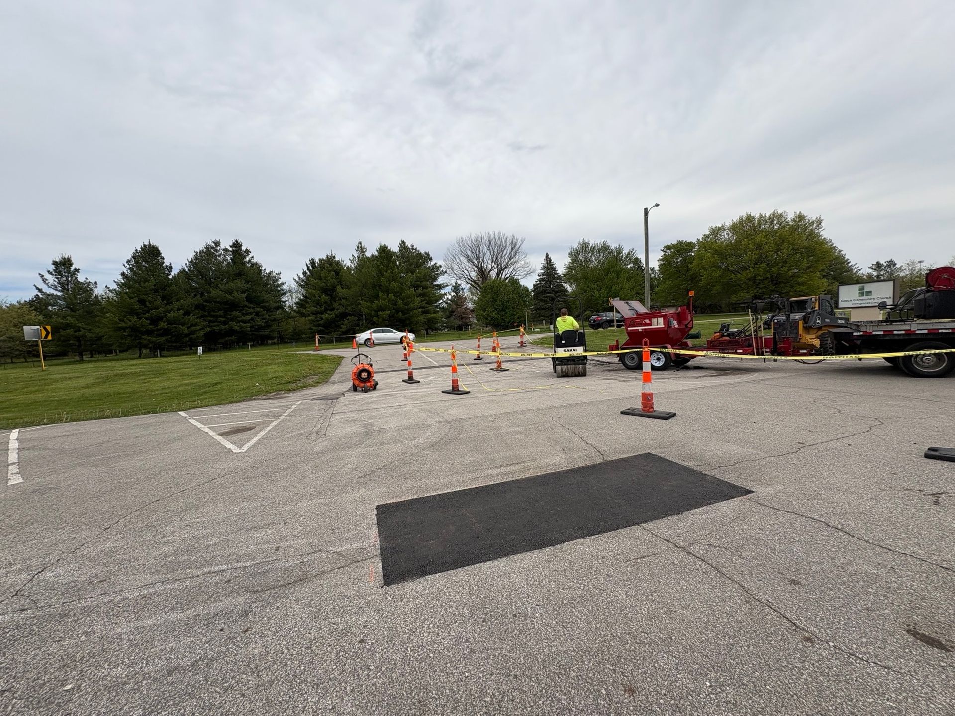 Roadwork area with orange cones and a red lift on a paved lot under an overcast sky