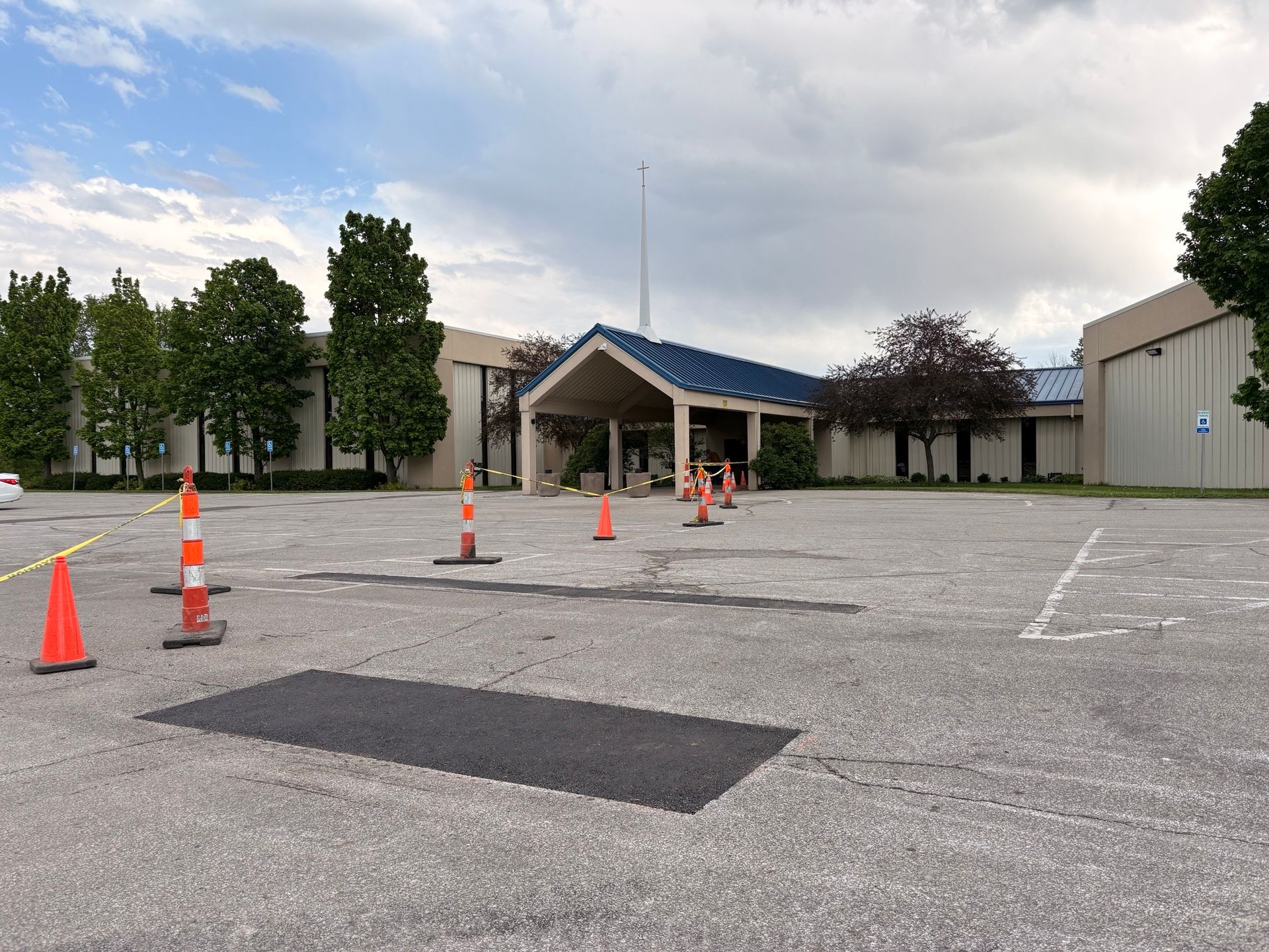 Empty parking lot with orange traffic cones and a building entrance under cloudy skies