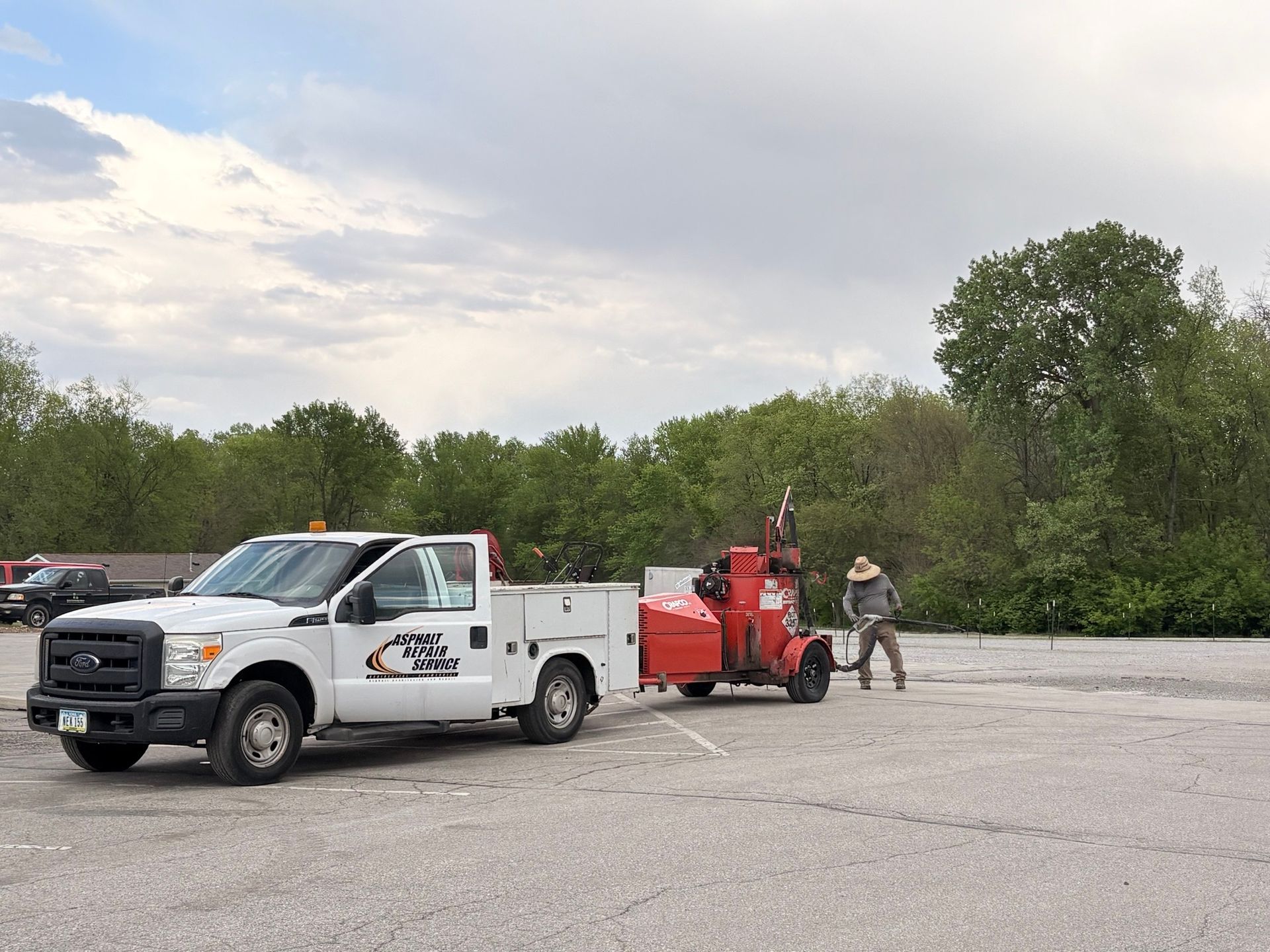 White utility truck towing a red equipment cart while two workers stand beside it in a parking lot