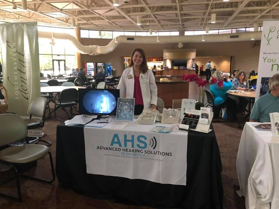 Woman at a health fair booth for Advanced Hearing Solutions, with hearing aids displayed and a visual of ear canal on screen.