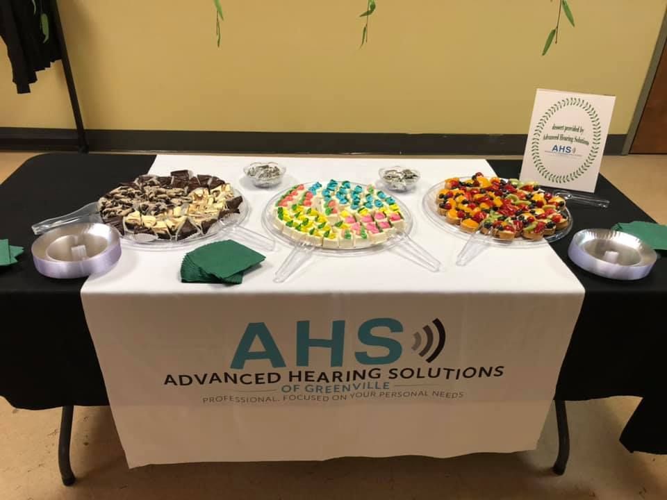 A table with treats and an AHS sign. A black tablecloth, white banner, and sweets.