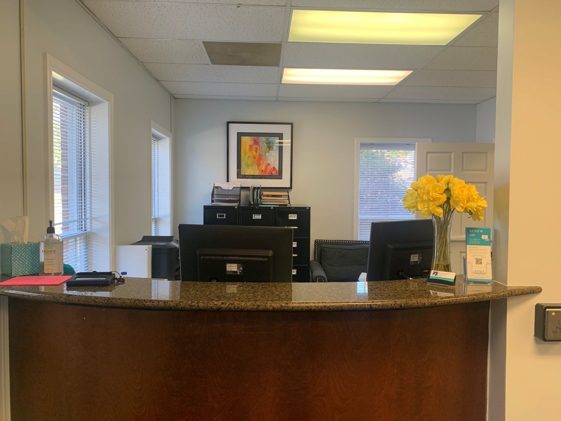 Reception area with a dark wood counter, computer monitors, and a floral arrangement.