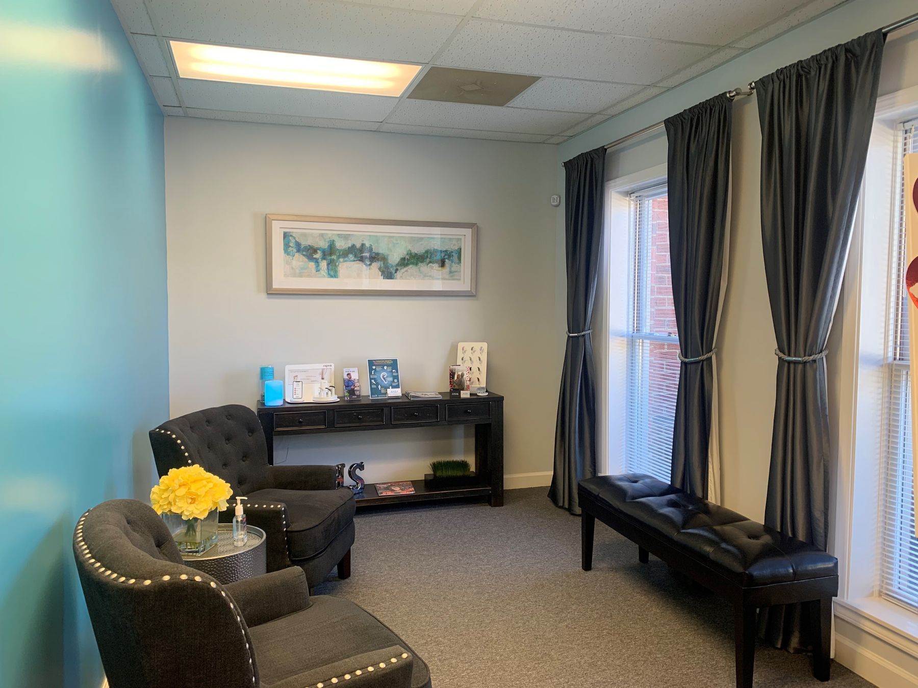 Waiting room with two armchairs, a bench, and a table with decorations; aqua and gray walls, gray carpet.
