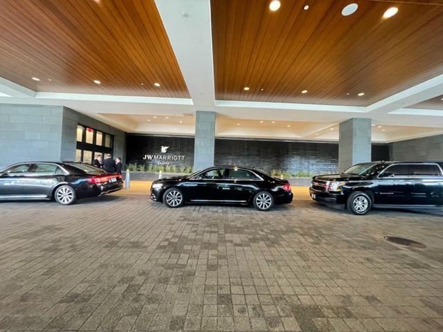 Three black luxury sedans parked under a covered hotel entrance with wood ceiling panels.