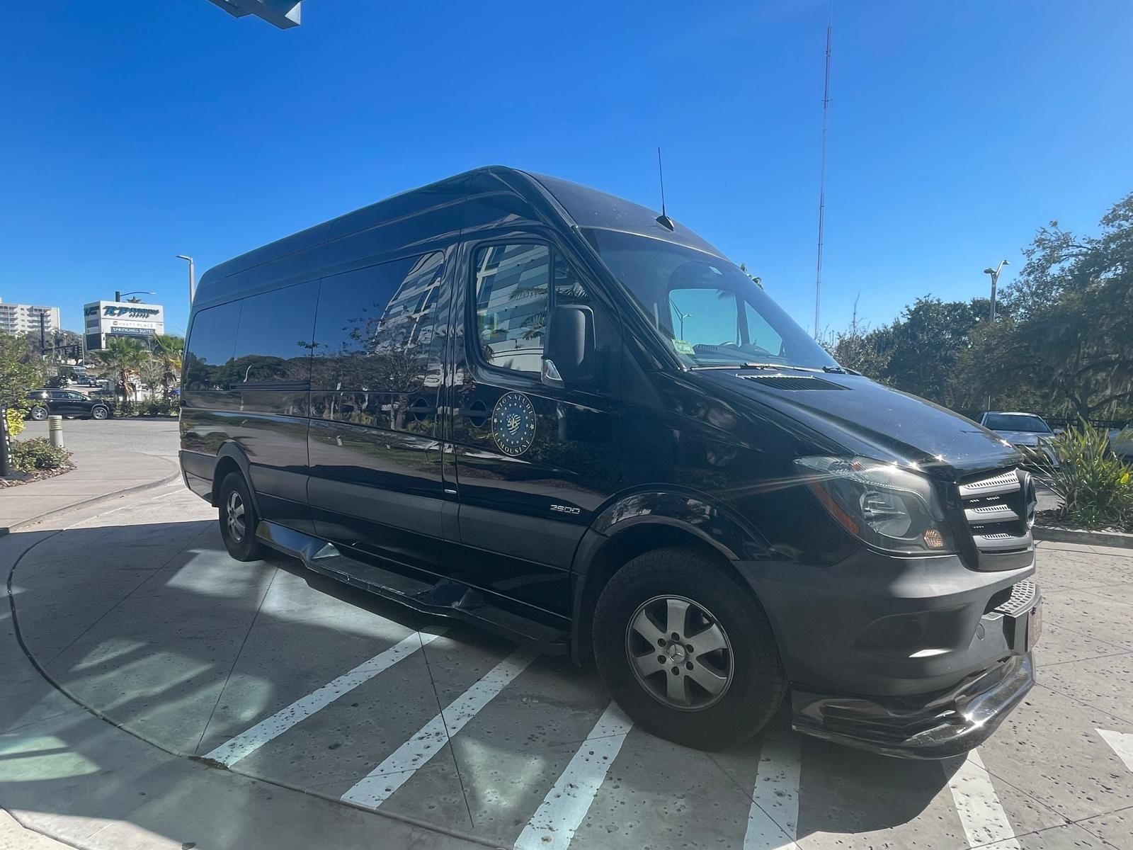 Black passenger van on a sunny street, angled over white road markings near a curb.